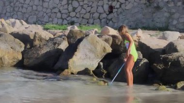 Benidorm, İspanya 'da Poniente sahilinde balık ya da yengeç yakalamaya çalışan yetişkin bir kız. Aile tatili konsepti. Yaz tatili konseptinin tadını çıkarın. Yüksek kalite 4K görüntü.