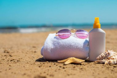 Güneş gözlüğü, havlu, güneş kremi ve kumlu sahilde deniz kabukları..