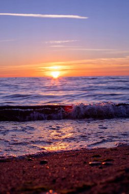 Kumsalda sakin okyanus dalgaları üzerinde canlı gün batımı.