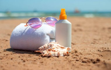 Güneş kremi, güneş gözlüğü ve kumlu sahilde havluyla deniz kabuğu..