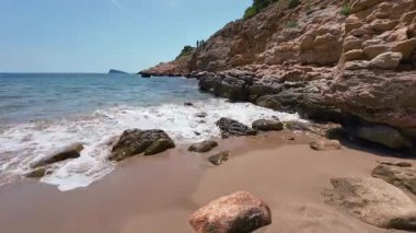 Zaman çizelgesi, Benidorm, İspanya 'da insansız bir sahile yakın. Körfez, sahil kıyısının arkasında yer alıyor. Dalgalar plaj sahili görüntülerinde kayalara çarpıyor.