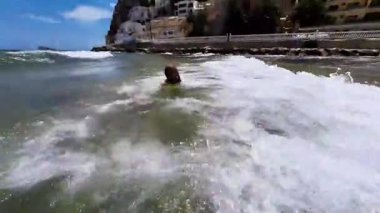 Maceracı küçük kız güneşli bir günde güzel bir sahilde dalgaların tadını çıkarıyor. Yüksek kaliteli FullHD görüntüler