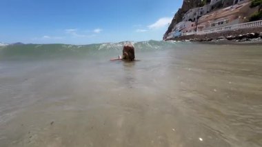 Küçük kız okyanus dalgalarının tadını çıkarıyor ve güneşli sahilde yemek yiyor. Yüksek kaliteli FullHD görüntüler