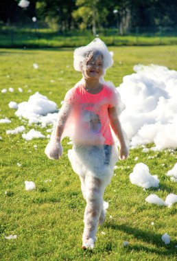 Güneşli bir günde dışarıda sabun köpükleriyle oynayan neşeli çocuk..