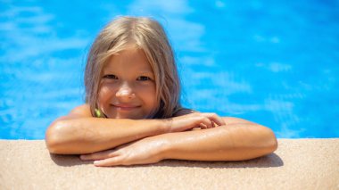 Neşeli bir çocuk havuzun kenarına eğiliyor, neşeyle gülümsüyor suyun üzerindeki güneş ışığı gibi. Ortam canlı ve davetkar, bir yaz günü için mükemmel..