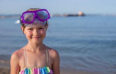 Güneşli bir günde gözlüklü genç bir kız kumsalda gülümsüyor..