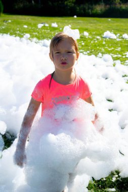 Açık hava köpük partisinde pembe tişört ve köpüklerle oynayan genç bir kız..