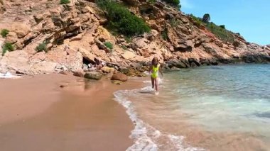 Yazın kayalık kayalıkların yanında kumsalda neşeyle koşan bir çocuk. Yüksek kalite 4k görüntü