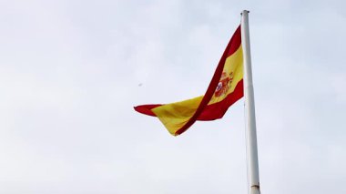 İspanyol bayrağı hafif meltemde bulutlu gökyüzüne doğru zarif bir şekilde dalgalanıyor. Yüksek kalite 4k görüntü