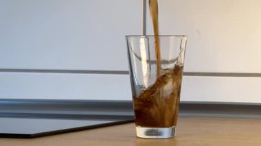 Bardak kolayla dolu, köpüklü koyu renkli bir içecek.