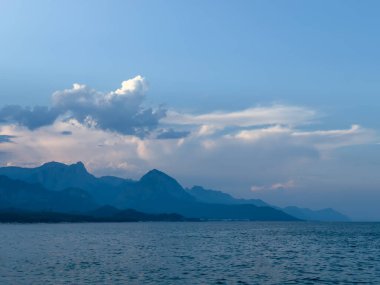 Gün batımından önce deniz, arka planda dağlar ve bulutlarla. Gökyüzünün kırmızı ve turuncu tonları. Yüksek kalite fotoğraf