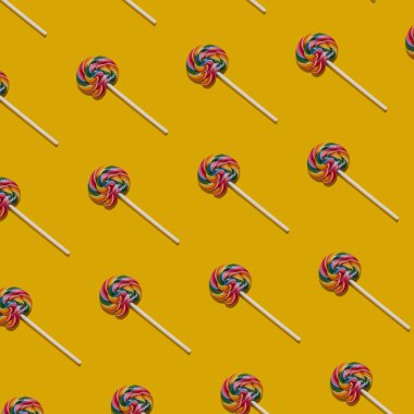  Sarı arka planda renkli lolipopların deseni. Yaratıcı şeker konsepti. Renkli tatlı yemek geçmişi. Yüksek kalite fotoğraf