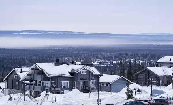 İskandinav dağ köyündeki karlı ahşap evler karla kaplı geleneksel ahşap kulübeler, uzak tepeler ve açık bir gökyüzünün altındaki ormanlarla çevrili engin kış manzarası..