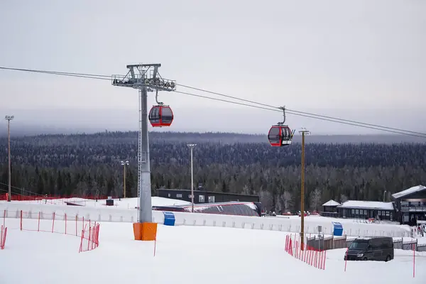 Göz kamaştırıcı manzarası olan iki kırmızı gondol iki kırmızı teleferik, karlı bir kayak merkezinin üstündeki rotalarında ilerliyor. Arka plandaki nefes kesici kış manzarası yuvarlanan tepeleri de kapsıyor..