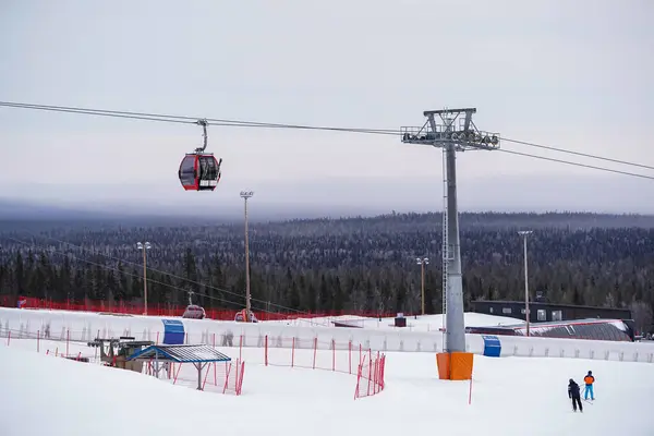 Kırmızı gondol, karlı alp otelinin üzerinde süzülüyor tek bir kırmızı teleferik, karla kaplı yamaçlar ve yoğun yeşil ormanlarla çevrili bir kış kayak merkezi üzerinde süzülüyor.. 