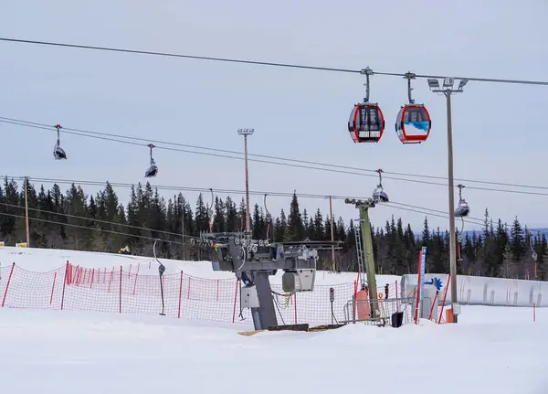 Kayak merkezinin gondolları karlı arazinin üzerinden geçerken iki kırmızı gondol bir kış otelinin üstünde yan yana hareket eder. Karla kaplı yamaçlar, güvenlik çitleri.