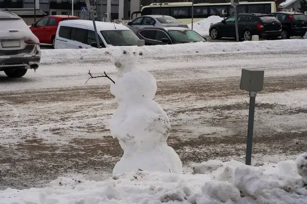Karlı bir otoparkta eriyen bir kardan adam buz gibi bir otoparkta kar yığınları ve soğuk bir kış gününde park halindeki arabalarla duruyor..