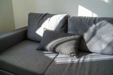 Doğal ışık altında dekoratif yastıklı modern kanepe. Pencerenin gölgeleri şık iç köşelerde rahat ve huzurlu bir atmosfer yaratıyor..