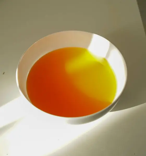 Basit bir beyaz kasedeki canlı kırmızı ve sarı jöle, minimum bir masa yüzeyindeki güneş ışığı ile aydınlatılır, yemek fotoğrafçılığı, tasarım veya menü çizimi için mükemmeldir..