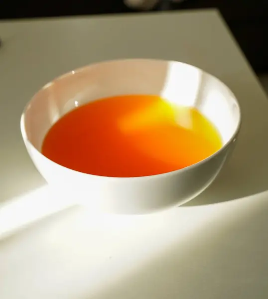 Parlak turuncu jöleli tatlı, parlak beyaz bir kasede servis edilir, açık renkli bir masada güneş ışığıyla yakalanır. Yemek ve minimalizm kavramları için mükemmel..