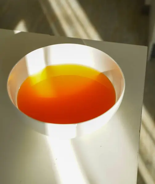 Bir kase kırmızı ve sarı bitkisel çay dramatik pencere ışığıyla aydınlatılıyor. Gölge ve renklerin karşıtlığı huzurlu, samimi ve doğal bir iç mekan yaratıyor..