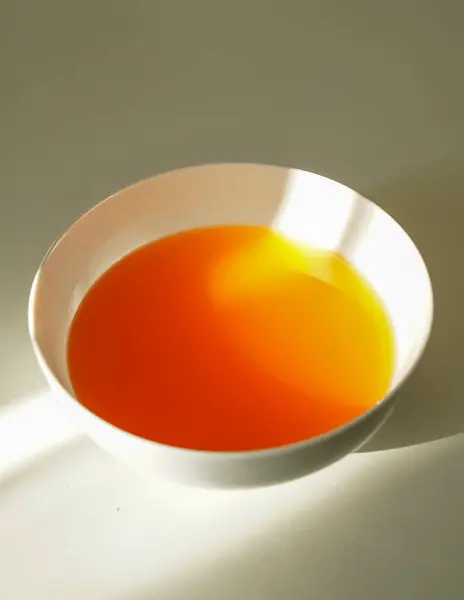 Beyaz bir seramik kasede parlak turuncu ve sarı jöle, güneş ışığının altında parlıyor. Temiz gıdaların görüntüsü için yukarıdan yumuşak bir ışık yüzeyinde yakalanır..