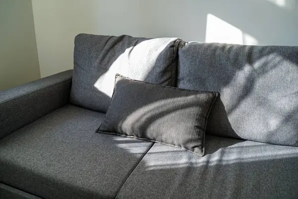 Doğal ışık altında dekoratif yastıklı modern kanepe. Pencerenin gölgeleri şık iç köşelerde rahat ve huzurlu bir atmosfer yaratıyor..