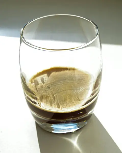İçinde espresso izleri olan boş bir bardağın yakın plan çekimi dramatik güneş ışığı ve gölge yansımaları olan beyaz bir pencere pervazında otururken minimalist bir ruh hali yaratıyor..