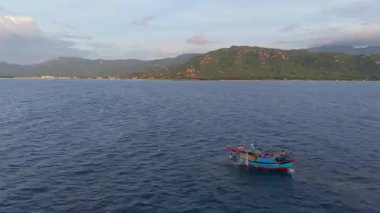 Okyanustaki balıkçı teknesinin havadan görünüşü, ağlarla çalışan balıkçılar, geleneksel geçim kaynakları ve Vietnam kıyılarının otantik yaşam tarzı. Balıkçılar denizde ahşap balıkçı teknesine ağlar çekiyor. 