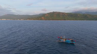 Okyanustaki balıkçı teknesinin havadan görünüşü, ağlarla çalışan balıkçılar, geleneksel geçim kaynakları ve Vietnam kıyılarının otantik yaşam tarzı. Balıkçılar denizde ahşap balıkçı teknesine ağlar çekiyor. 