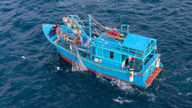 Okyanustaki balıkçı teknesinin havadan görünüşü, ağlarla çalışan balıkçılar, geleneksel geçim kaynakları ve Vietnam kıyılarının otantik yaşam tarzı. Balıkçılar denizde ahşap balıkçı teknesine ağlar çekiyor. 