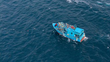Okyanustaki balıkçı teknesinin havadan görünüşü, ağlarla çalışan balıkçılar, geleneksel geçim kaynakları ve Vietnam kıyılarının otantik yaşam tarzı. Balıkçılar denizde ahşap balıkçı teknesine ağlar çekiyor. 