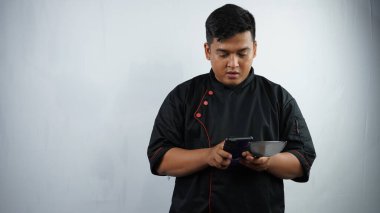Siyah arka planda yemek pişirirken elinde tablet olan Asyalı erkek şef.