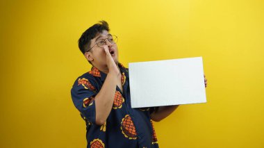 Beyaz gömlekli, gözlüklü, sarı arka planda bir hediye kutusu tutan Asyalı bir adam. yüksek kaliteli fotoğraf