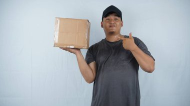 Genç yakışıklı Asyalı bir adam elinde siyah bir karton kutu tutuyor ve beyaz bir arka plana işaret ediyor, teslimat kavramı.