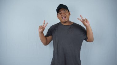 Mutlu Asyalı genç adam zafer jesti ile zafer gösteriyor. Gri arkaplanda izole edilmiş.
