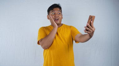 Asyalı genç ve yakışıklı bir adamın portresi günlük kıyafetler giyiyor, cep telefonunu el hareketleriyle kullanıyor, beyaz arka planda duruyor.