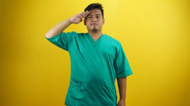 Sarı arka planda duran yeşil üniformalı Asyalı genç adam..
