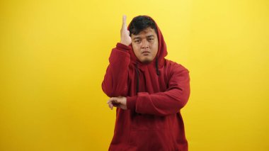 Kırmızı ceketli ve kazaklı Asyalı adam sarı kapüşonlu ve üzgün görünüyor.