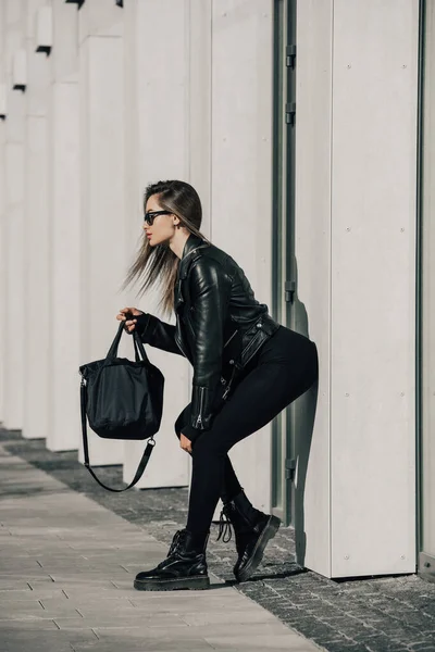 时尚的年轻女性 身穿紧身长袖紧身衣 身穿一身黑色皮夹克 脚跟平整 站在城市街道上 — 图库照片