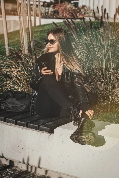 街上的一个女人用手机 网上购物 使用流动应用系统 美丽的女人 身穿黑色皮夹克和西服 — 图库照片