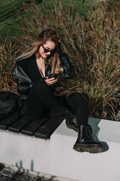 A woman on the street uses a mobile phone. online shopping. use of mobile applications. beautiful woman with long hair in a black leather jacket and bodysuit