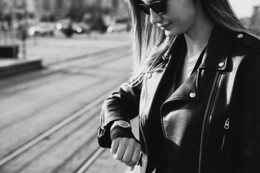 Tramvay istasyonunda duran ve tramvay bekleyen genç bir kadın. Siyah deri ceket giyiyor.