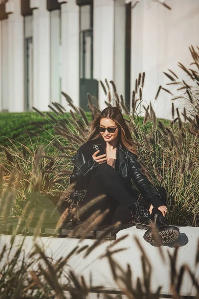 街上的一个女人用手机 网上购物 使用流动应用系统 美丽的女人 身穿黑色皮夹克和西服 — 图库照片