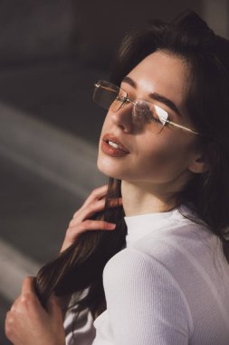 Neşeli, mutlu, güzel, dişlek bir kadının fotoğrafı. Güneşin tadını çıkaran güneş gözlüğü takıyor. Gömlekli şehir dışında.