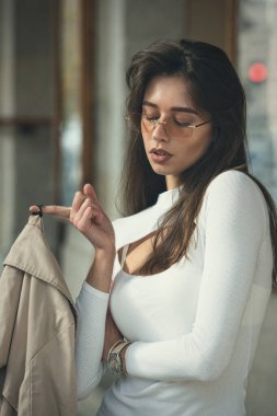 Güneş gözlüklü, beyaz bluzlu, elinde bej ceketi olan güzel esmer kız. Moda anlayışı çok şık..