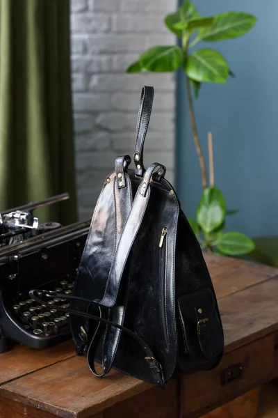 Black shiny leather casual backpack on a wooden table. Indoor photo