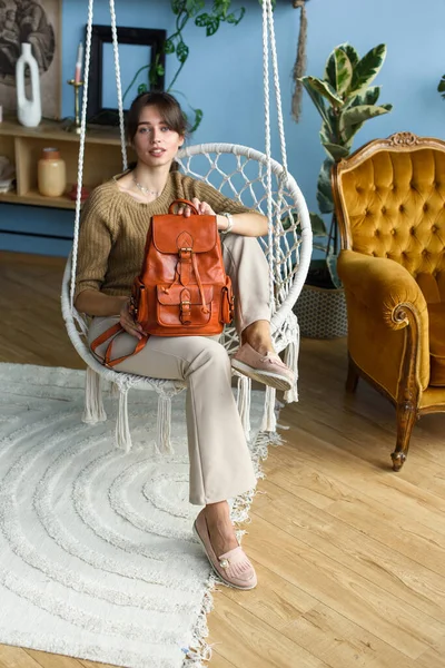 베이지 바지와 올리브 스웨터를 아름다운 소녀가 오렌지 가방을 의자에 포즈를 — 스톡 사진