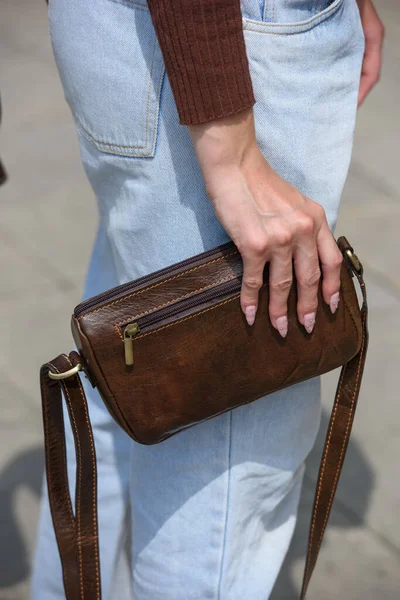 close-up photo of small brown leather bag in a woman hands. outdoors photo.