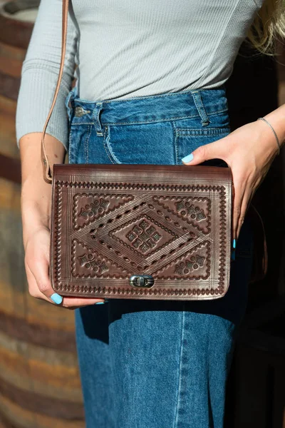 small brown womens leather bag with a carved pattern. street photo